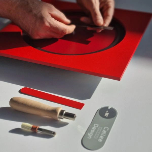 Hands assembling the contrasting elements of the red KAM Lava wall clock in the atelier