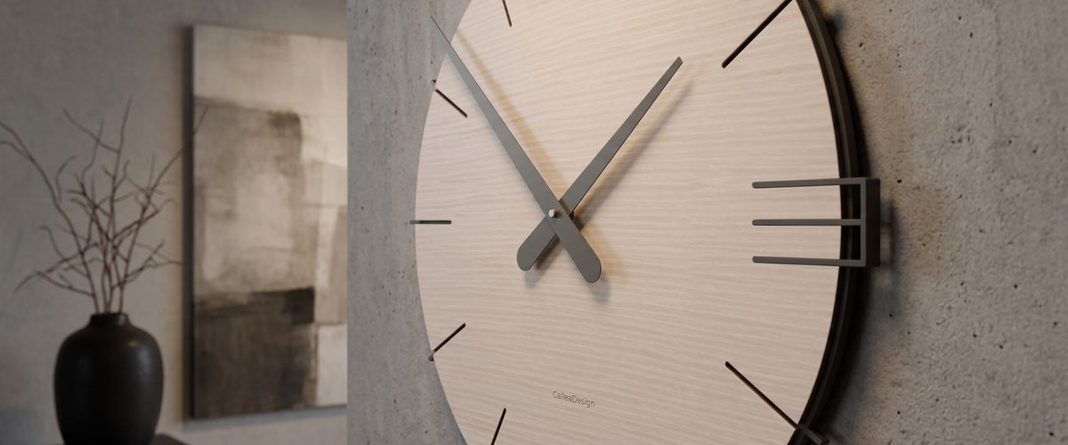 Dettaglio di un orologio da parete CalleaDesign con quadrante in legno chiaro e lancette scure in un ambiente contemporaneo